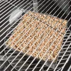 A close-up view of a stainless steel smoker box filled with wood pellets, placed on a grill grate. Produktbild-Vorschau