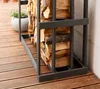 A close-up view of a dark gray metal firewood rack filled with cut logs, placed on a wooden deck next to a wall. Podgląd zdjęcia produktu