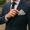 A man in a suit is adjusting a pocket square in his suit jacket. Produktbild-Vorschau