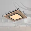 A square ceiling light with a wood-effect frame and a black border around a central illuminated panel, shown attached to a ceiling. Dimensions are indicated with lines and text. Produktbild-Vorschau