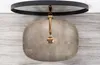 A top-down view of a beige marble vessel sink with a gold faucet, mounted on a wall with a wood-like texture, and a black circular mirror above. Anteprima dell’immagine prodotto