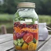 A mason jar filled with salad ingredients, placed on a wooden table outdoors. Podgląd zdjęcia produktu