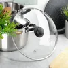 A glass lid is placed over a stainless steel pot, with a wooden spoon and green plant visible. Produktbild-Vorschau