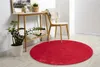 A red circular rug is placed on a light wooden floor in a room with a small wooden table and a chair. Produktbild-Vorschau