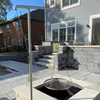 A stainless steel grill stand with a hanging grill grate is set up on a patio next to a house. Podgląd zdjęcia produktu