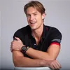 A man wearing a black polo shirt with red accents and a watch is posing for a product shot. Produktbild-Vorschau