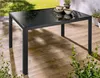 An outdoor table with a glass top on a wooden deck, surrounded by plants. Produktbild-Vorschau