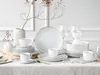 A neatly arranged table setting with white porcelain dinnerware and gold accents. Produktbild-Vorschau