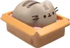 A Pusheen the cat figurine is sitting in a cardboard box filled with pink packing peanuts. Produktbild-Vorschau