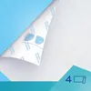 A close-up view of a white, textured material, possibly a disposable pad or liner, with a corner peeled back to reveal printed text and blue graphic elements. Produktbild-Vorschau