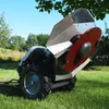 A rotary mower is shown in a grassy outdoor setting with trees and a blue sky in the background. Produktbild-Vorschau