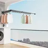 A balcony with a washing machine and a retractable clothes drying rack mounted on the wall, with clothes hanging on it. The background shows a cityscape under a blue sky. Produktbild-Vorschau