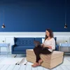 A woman is sitting on a folded mattress and working on a laptop in a living room setting. Voir les images du produit