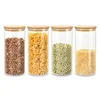 Four glass storage jars with bamboo lids, each filled with different dry goods: beans, pasta, peas, and rice. Produktbild-Vorschau