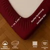 A close-up of a burgundy fitted sheet corner, showing the elastic edge and some product feature icons and text. Produktbild-Vorschau