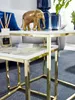 A close-up shot of two nested side tables with gold metal frames and white marble-effect tops, featuring decorative items like a golden elephant figurine, a blue vase, and a diffuser. Produktbild-Vorschau