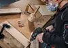A person is using a drill to make a hole in a piece of wood on a workbench. Voir les images du produit