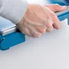 A person's hand is shown gripping a blue paper cutter. Anteprima dell’immagine prodotto