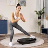 A woman is exercising on a vibration plate in a room. Voir les images du produit