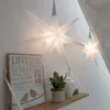 Two star-shaped LED lights hang in a room, one larger than the other. A wooden shelf below holds a framed sign with text, a potted plant, and a decorative jar. Produktbild-Vorschau