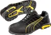 A pair of black and yellow Puma safety shoes shown from a diagonal angle, with one shoe placed slightly behind and above the other, showcasing the sole. Voir les images du produit