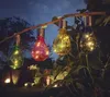 Four solar-powered LED light bulbs in different colors (green, red, yellow, blue) are hanging from a tree branch in a garden at dusk. Produktbild-Vorschau