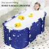 A young girl is taking a bath in a portable bathtub filled with bubbles and rubber ducks. Produktbild-Vorschau