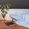 A light blue fitted sheet is draped over a white mattress, with a vase of greenery and white flowers and a black notebook on a wooden surface in the foreground. Anteprima dell’immagine prodotto