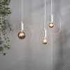 Three modern pendant lights with Edison-style bulbs hang against a gray wall, with a plant on the left. Podgląd zdjęcia produktu