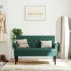 A dark green tufted bench is placed in a hallway with a coat hanging on a wall hook, a plant, a mirror, and shoes on the floor. Produktbild-Vorschau