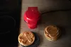 A red mini waffle maker on a wooden surface with freshly made waffles. Produktbild-Vorschau