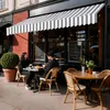 A couple sits at a table outside a cafe under a striped awning. Náhled obrázku produktu