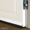 A close-up view of a white door with a black brush seal attached to the bottom, resting on a wooden floor. Produktbild-Vorschau