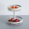 A two-tiered fruit basket filled with fruits, placed on a countertop against a tiled wall. Podgląd zdjęcia produktu