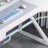 A close-up view of a modern white gaming desk with a blue and white keyboard, a gray mousepad, and a white mouse. The desk has integrated lighting and a metal frame. The background shows gray curtains and a patterned carpet. Náhľad obrázku produktu