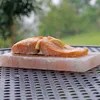 A piece of salmon is cooked on a salt block, placed on an outdoor table. Produktbild-Vorschau