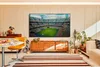 A living room scene with a large television displaying a soccer match, a wooden sideboard, a dining table with chairs, and a sofa. Produktbild-Vorschau