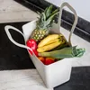 A reusable grocery bag filled with fresh produce, including a pineapple, bananas, bell peppers, and leeks, placed on a patterned floor. Náhled obrázku produktu