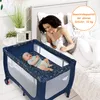 A mother is lying in bed next to a baby in a travel crib. Anteprima dell’immagine prodotto