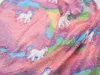 A close-up of a soft, fluffy blanket with a rainbow tie-dye pattern and unicorn prints. Anteprima dell’immagine prodotto