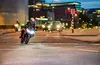 A motorcycle rider on a street at night with city lights in the background. Náhľad obrázku produktu