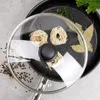 A glass lid with a stainless steel rim is placed over a frying pan. The lid has a black handle and contains three nests of uncooked pasta. The pan contains bay leaves and some greenery. Peppercorns are scattered around the lid. Voir les images du produit