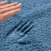A hand pressing into a soft, blue bath mat, showing its texture and plushness. Anteprima dell’immagine prodotto