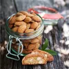 A jar of almonds and two biscotti on a wooden surface. Produktbild-Vorschau