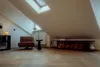 A cozy attic room with a skylight, a comfortable armchair, and a fireplace stocked with firewood. Produktbild-Vorschau
