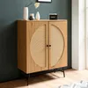A wooden sideboard with rattan woven doors stands against a dark green wall, with decorative items on top. Produktbild-Vorschau