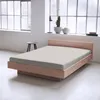 A bed with a light-colored fitted sheet in a room with large windows. Produktbild-Vorschau