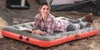 A woman is lying on an inflatable mattress outdoors, reading a book. A tent is visible in the background. Podgląd zdjęcia produktu