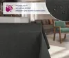 A dark gray tablecloth is draped over a table in a living room setting. In the background, a sofa and an armchair are visible. A close-up inset shows water droplets on the fabric. Produktbild-Vorschau