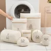 A collection of laundry bags of various sizes and shapes are arranged in front of a washing machine. A hand is reaching towards one of the bags. Produktbild-Vorschau